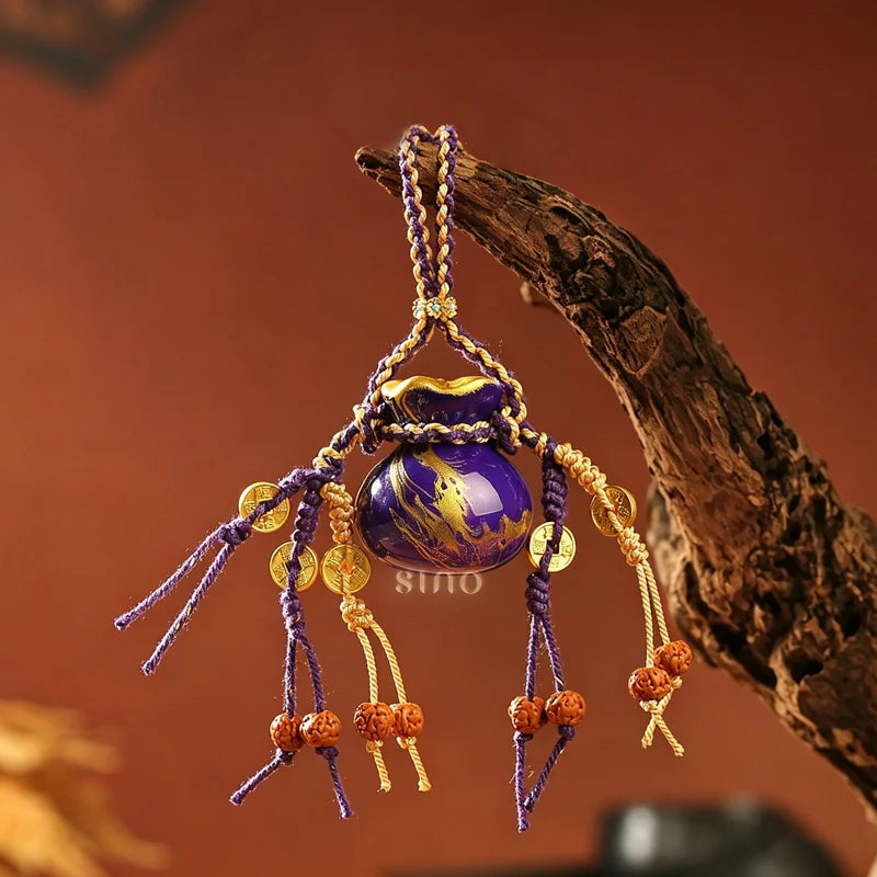 Gilded purple Daqi lacquer money pouch-shaped bag charm displayed hanging on a branch, with braided purple and gold cords, coin ornaments, and bead tassels.