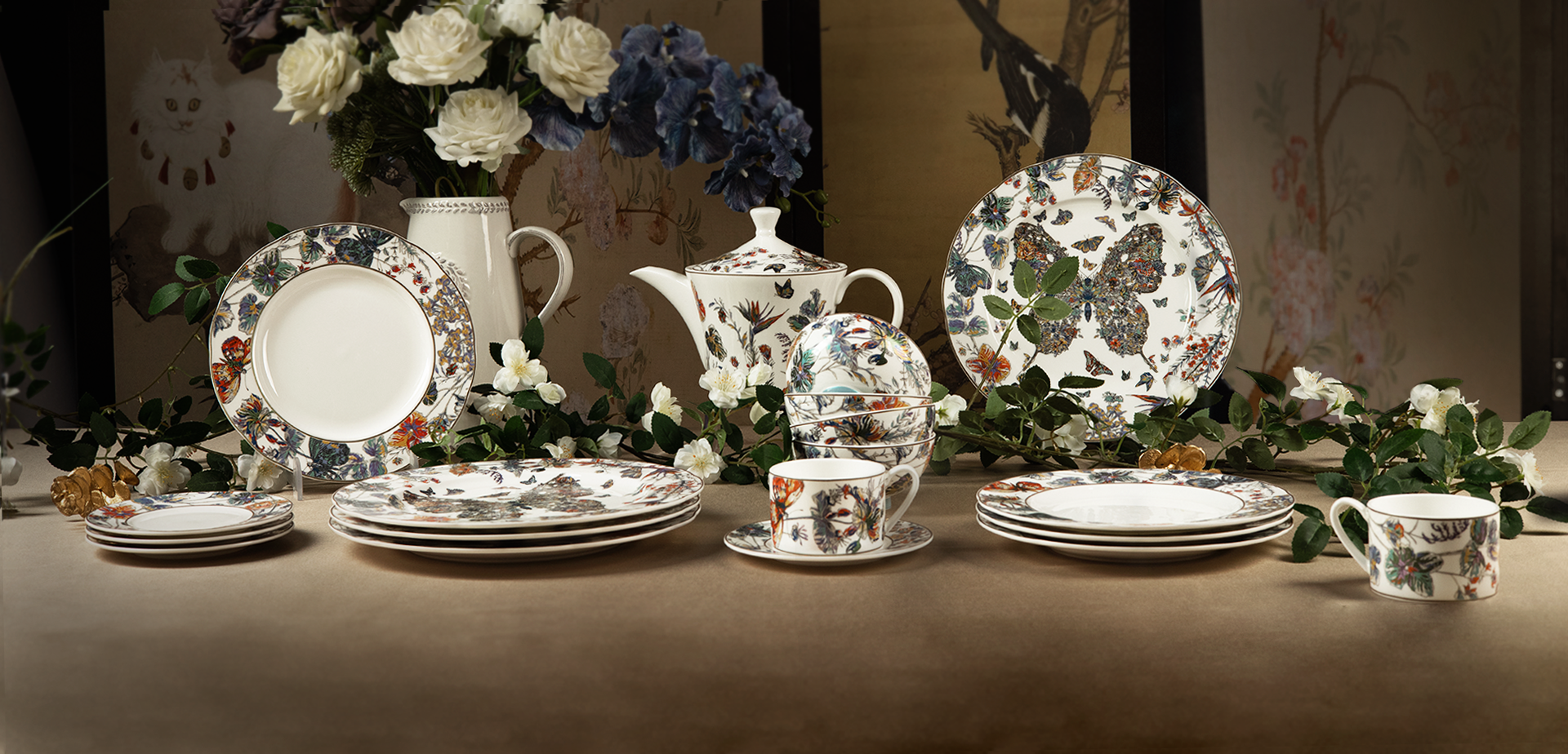 Luxurious table setting featuring our Golden Butterfly Dance series bone china—delicate butterfly and floral patterns adorn plates, a teapot, and cups, accented by fresh greenery and blooms.