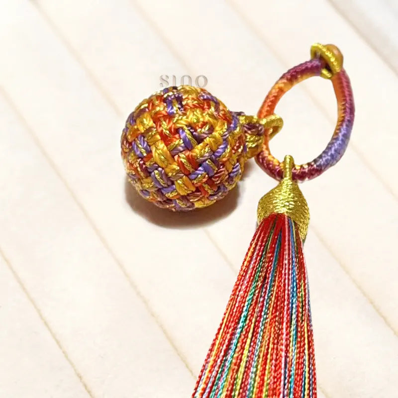 Close-up of the handmade Fire Fortune Ball tassel charm, showing the multicolor woven texture, braided loop, and silky rainbow tassel.