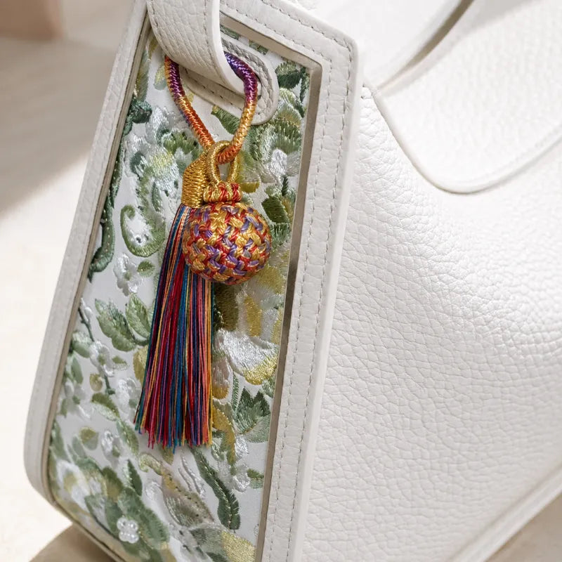 Handmade Fire Fortune Ball tassel bag charm displayed on a white handbag with a colorful woven ball and long rainbow tassel.