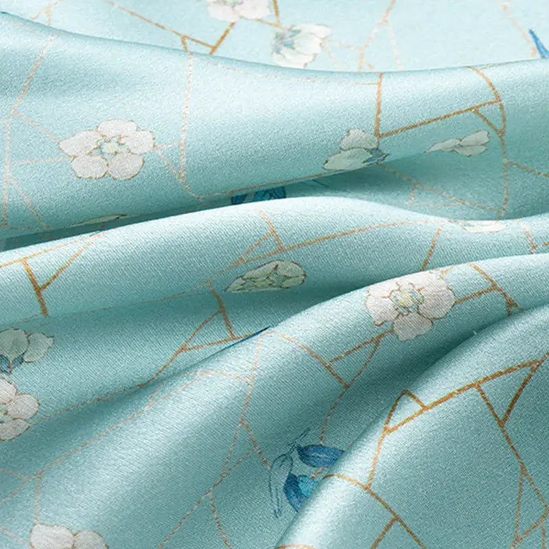 Close-up of smooth mulberry silk fabric with plum blossoms, bamboo leaves and gold ice-crack lines on the square scarf.