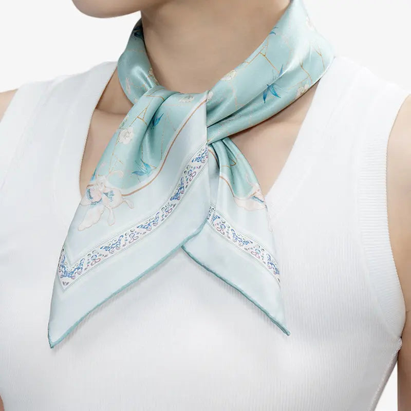 Woman wearing the blue-green Ice-Crack Plum & Bamboo Mulberry Silk Square Scarf tied elegantly around the neck.