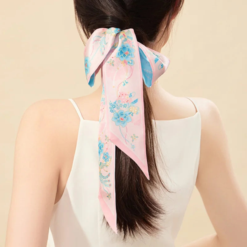 Woman styling the Jeweled Phoenix & Peony Mulberry Silk Twilly as a pink floral ponytail hair scarf.