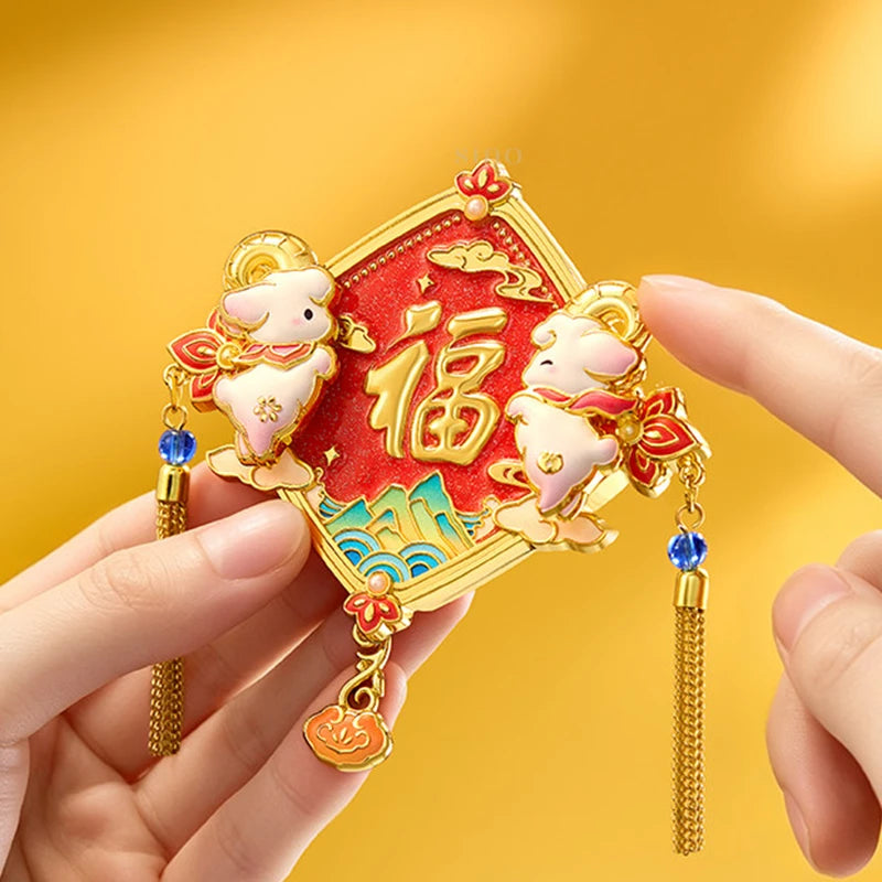 Hand holding a red and gold Year of the Goat fridge magnet with the Chinese Fu character, two cute sheep, blue accents, and hanging tassels.