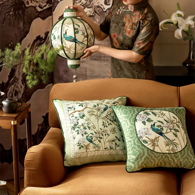 Square-shaped luxury chinoiserie jade green decorative throw pillows arranged on a sofa, with a model standing behind holding a lantern pillow.