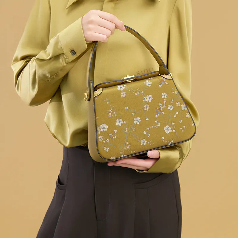 Model holding the Luxury Chinoiserie Song Brocade Magpie & Plum Blossom Handbag at chest level, with the other hand holding the strap.