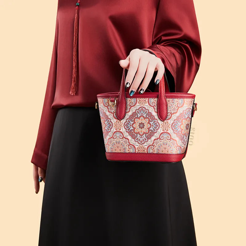 Side view of model carrying the luxury red Song brocade top-handle bag by hand with arm raised, showing the full texture and shape.
