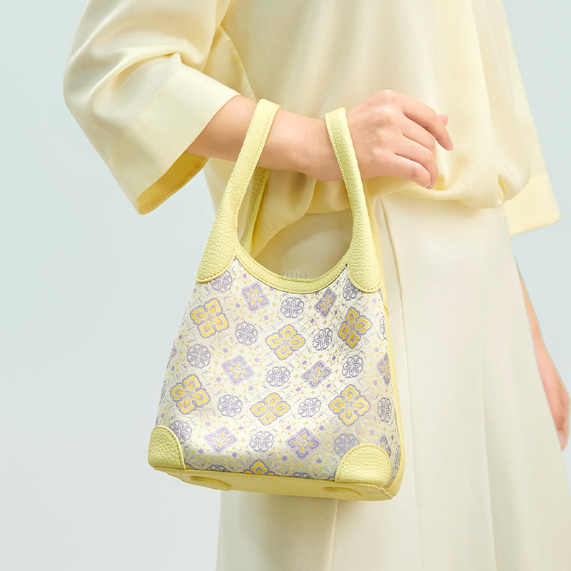 Model carrying the Luxury Shu Brocade Persimmon Calyx Motif Basket Tote Bag by hand, showing the light yellow leather handles and elegant basket tote shape.