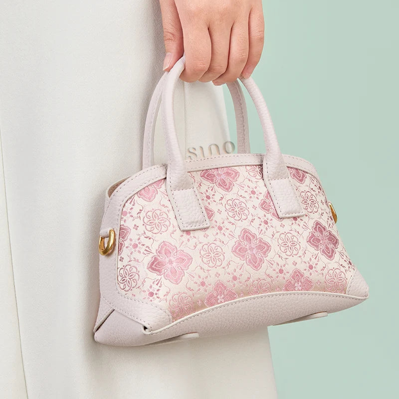 Model holding the Luxury Shu Brocade Pink Persimmon Calyx Leather Top Handle Bag by hand in a lifestyle setting.