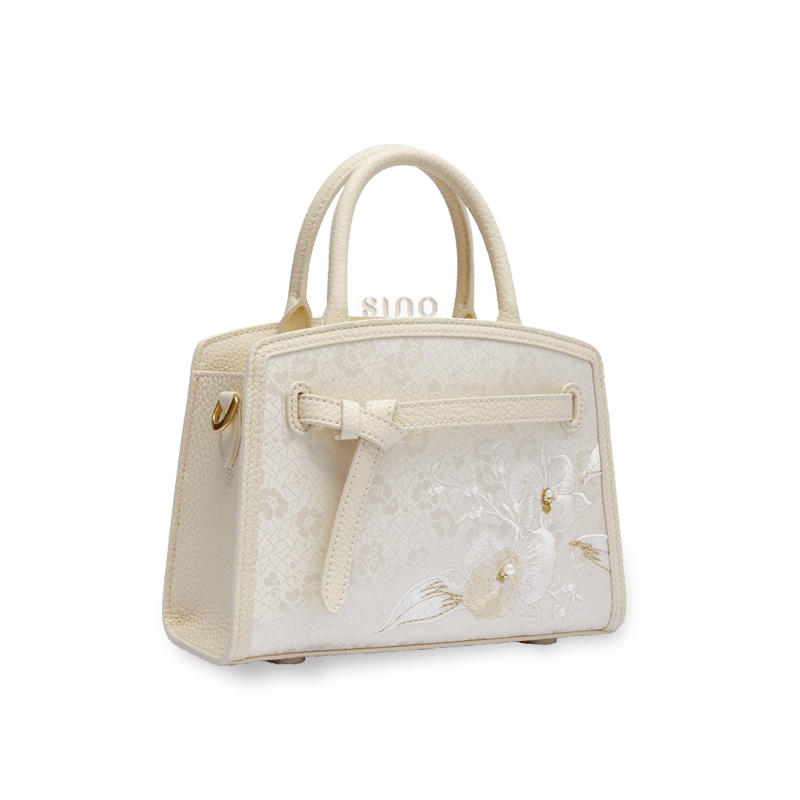Angled view of the Luxury Shuanglin Silk Orchid Butterfly Embroidered Leather Top Handle Bag showing its structured silhouette, top handle, and embroidered front panel.