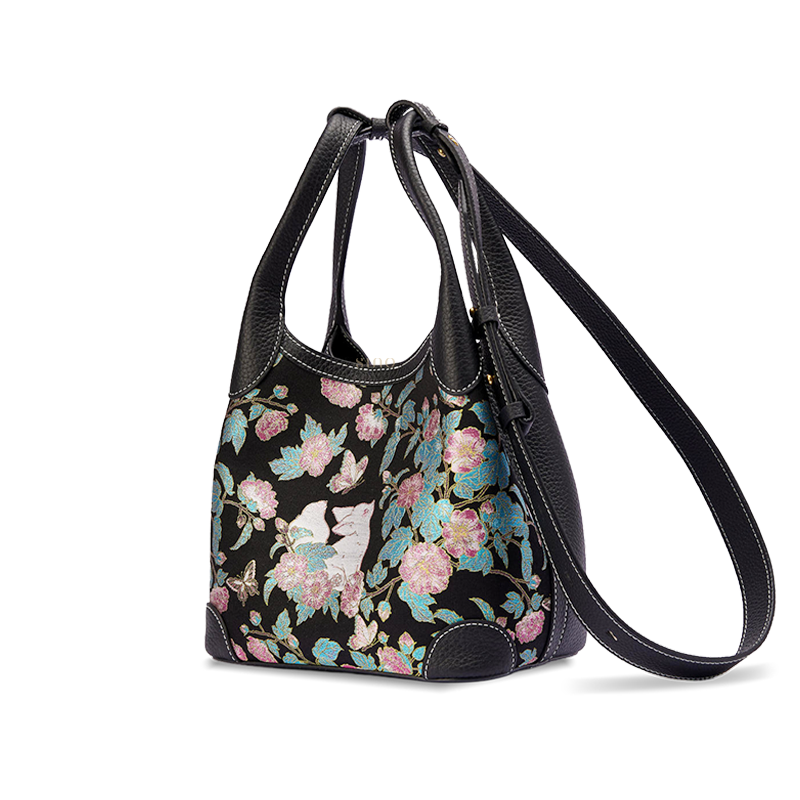 Angled view of the Luxury Song Brocade Butterfly and Auspicious Fox Basket Tote Bag with long strap, highlighting the black leather side panel and woven brocade design.