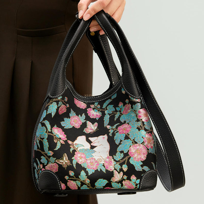 Close-up model view of the Luxury Song Brocade Butterfly and Auspicious Fox Basket Tote Bag, highlighting the colorful woven motif, black leather handles, and long strap.