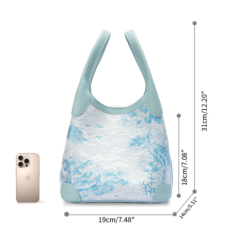 Size reference image of the Luxury Song Brocade Misty Mountain Forest Leather Basket Tote Bag, shown with a phone for scale and everyday carrying capacity.