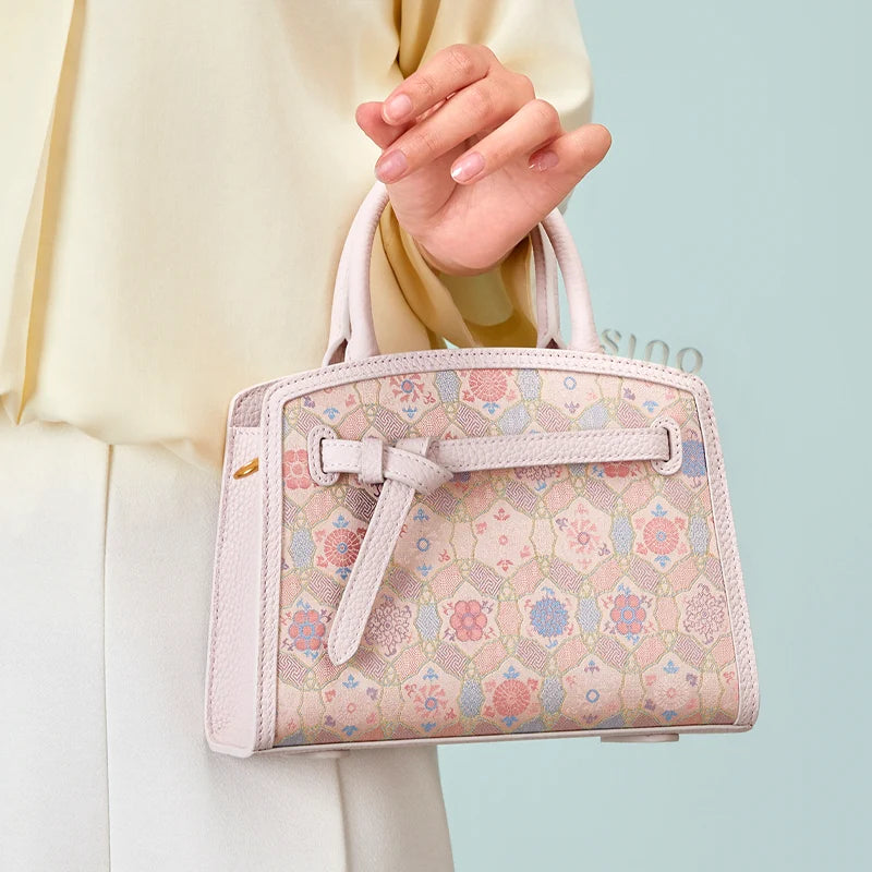 Model holding the Luxury Song Brocade Ruyi Longevity Motif Leather Top Handle Bag by hand in a lifestyle setting.