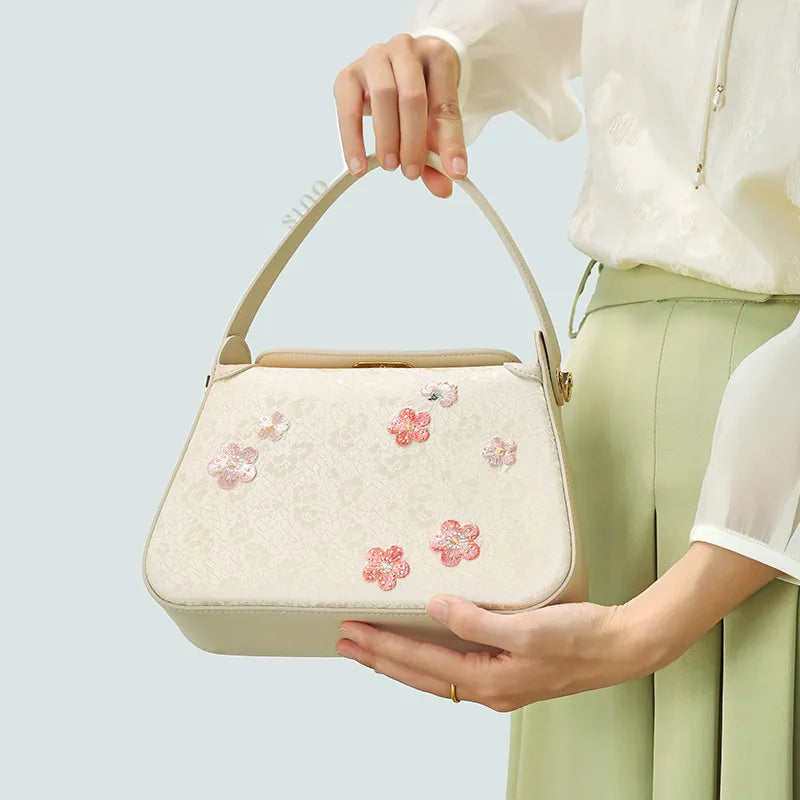 Model holding a plum blossom handbag with one hand on the handle and the other hand supporting the base.