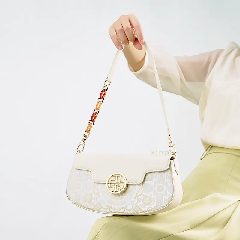 Model seated single hand holding octagonal brocade shoulder bag on knees.