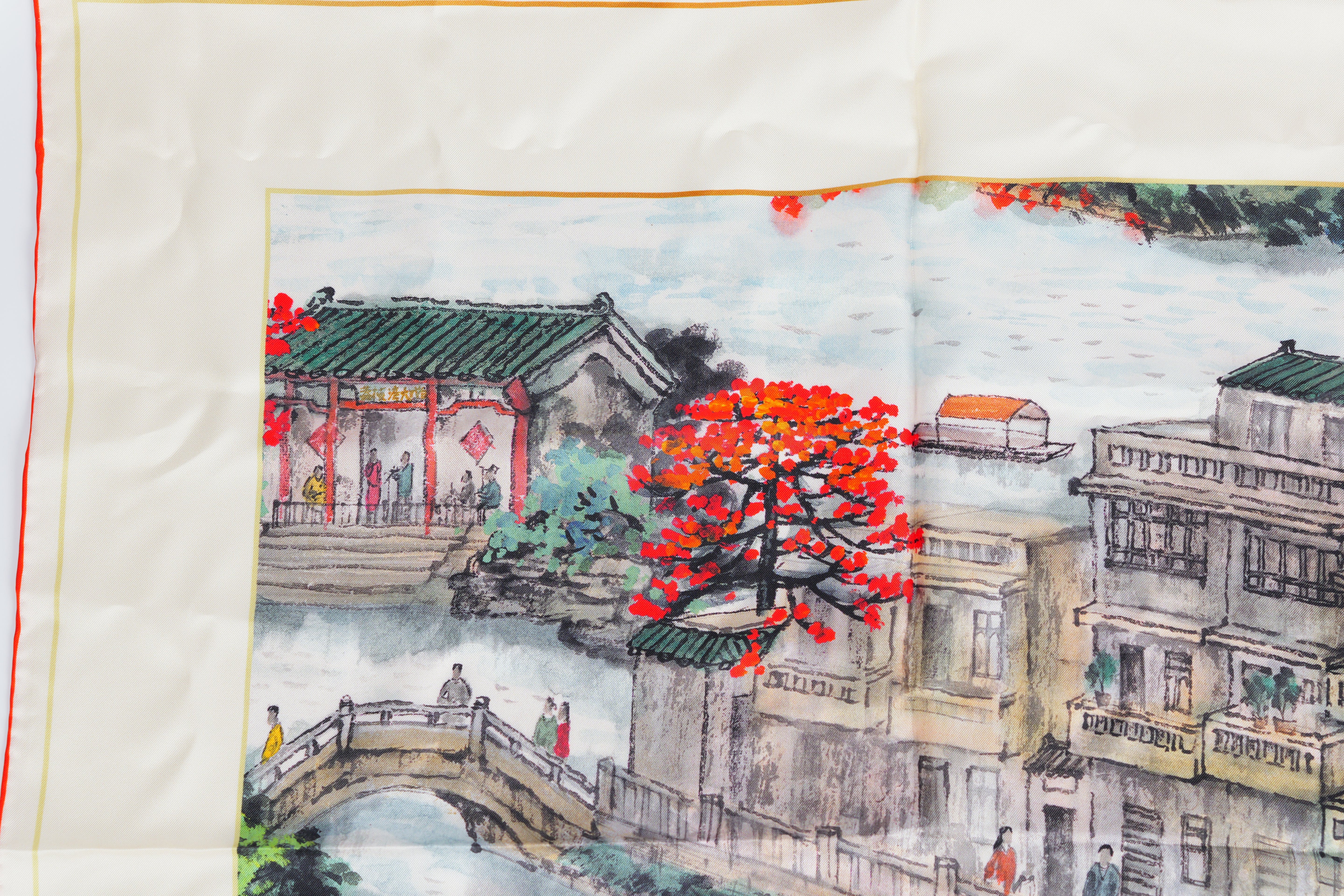 Close-up of Lychee Bay scarf's Chinoiserie embroidery: delicate bridges, willow trees, and porcelain-inspired patterns on premium silk.