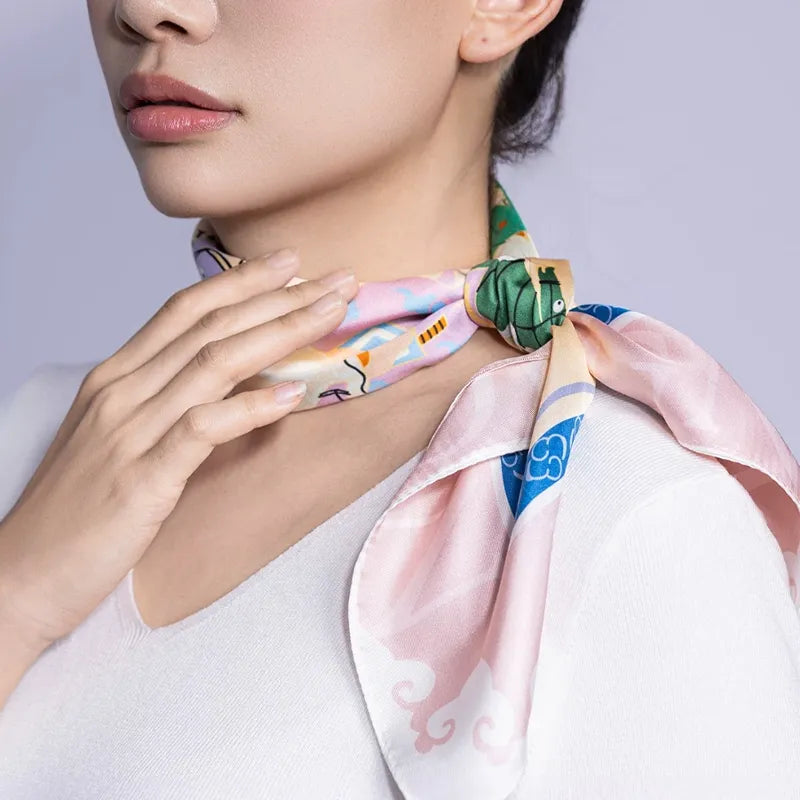 Model wearing the Nine Horses Print mulberry silk square scarf in a side neck knot with soft pink and blue border details.