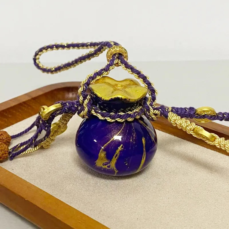 Close-up of the purple Daqi lacquer money pouch-shaped bag charm, showing the glossy lacquer finish, gilded patterning, braided cord wrapping, and decorative hanging details.