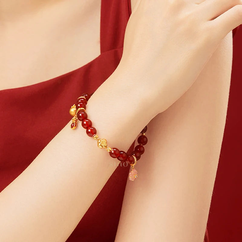 Red agate beaded lucky bracelet styled on the wrist with gold-tone charms, a Chinese New Year accessory that complements festive outfits and everyday looks.