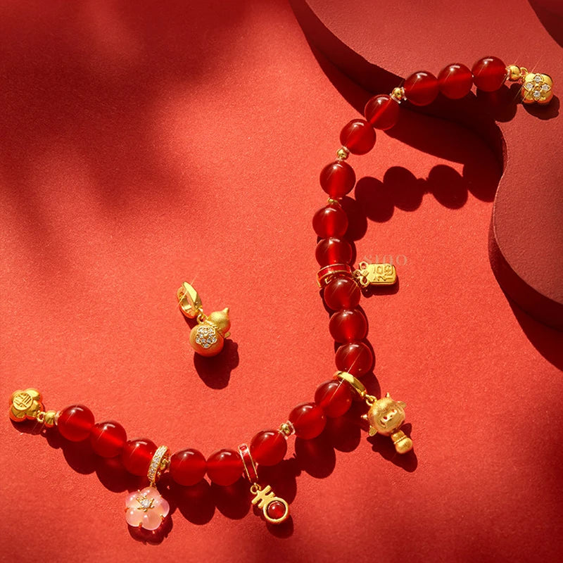Detailed view of the red agate bracelet's gold-tone charms, including a pink blossom, goat-inspired pendant and auspicious symbols, showcasing its Chinese New Year design.