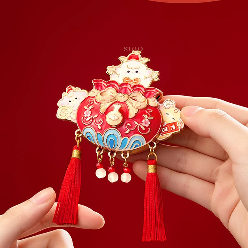 Hand holding a red and gold Chinese New Year fridge magnet decorated with cute sheep, lucky pouch motifs, pearl-like charms, and red tassels.