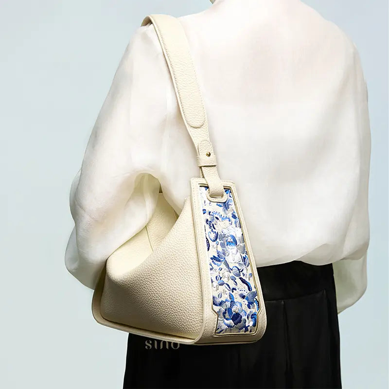 Woman wearing a beige leather shoulder bag with a blue SANLAN embroidered floral panel.