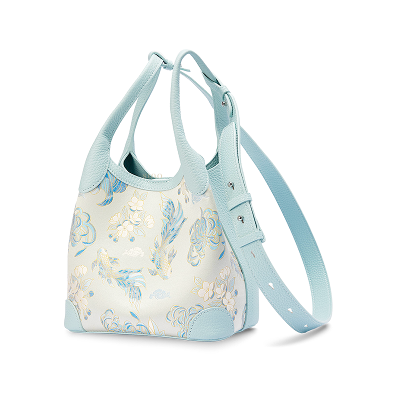 Angled view of the Luxury Shu Brocade Golden Fish & Flower Leather Basket Tote Bag with long strap, showing the light blue leather side panel and woven fish floral design.