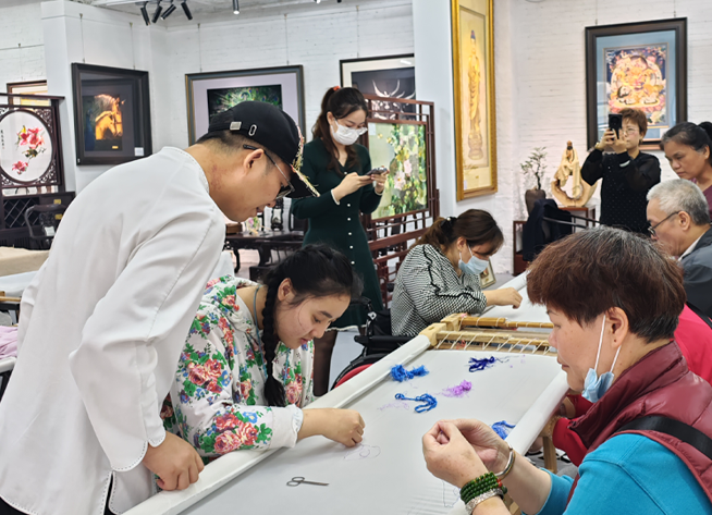 Canton Embroidery master Wang Xinyuan guides people with disabilities through hand embroidery techniques during a charitable craft class.