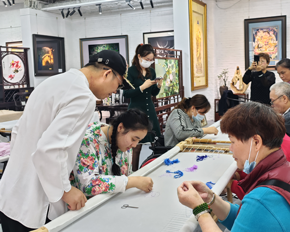 Canton Embroidery master Wang Xinyuan guides people with disabilities through hand embroidery techniques during a charitable craft class.