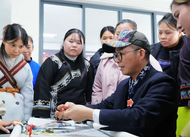 Canton Embroidery master Wang Xinyuan demonstrates hand embroidery techniques to Shui women artisans during a workshop in Guizhou, China.