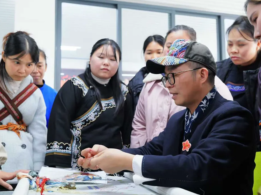 Canton Embroidery master Wang Xinyuan demonstrates hand embroidery techniques to Shui women artisans during a workshop in Guizhou, China.
