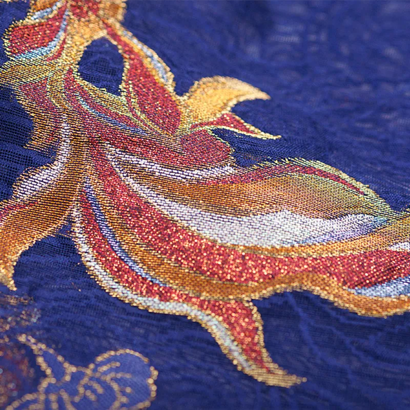 Detailed view of a colorful fish motif woven with shimmering gold threads against the deep blue Nanjing Yunjin silk brocade.