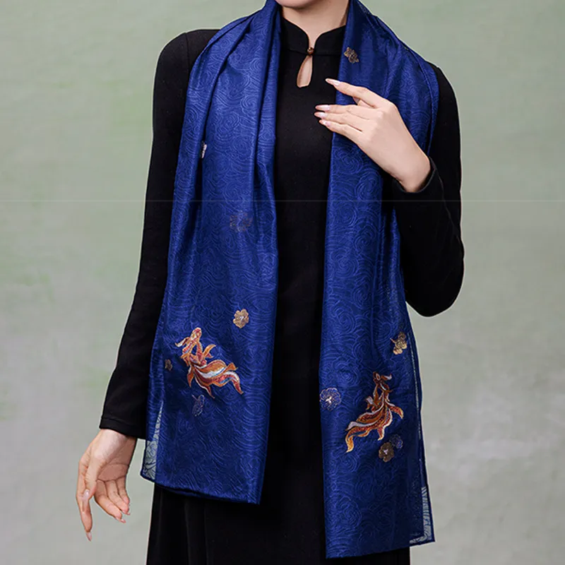 Model wearing a deep blue Nanjing Yunjin brocade mulberry silk shawl over a black outfit, featuring gold-thread fish and floral motifs.