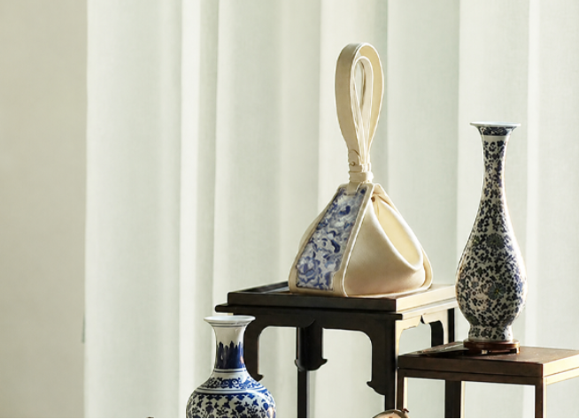 A cream SANLAN embroidered Zongzi bag displayed beside traditional blue-and-white porcelain vases.