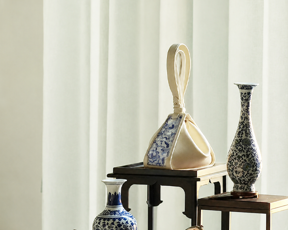 A cream SANLAN embroidered Zongzi bag displayed beside traditional blue-and-white porcelain vases.