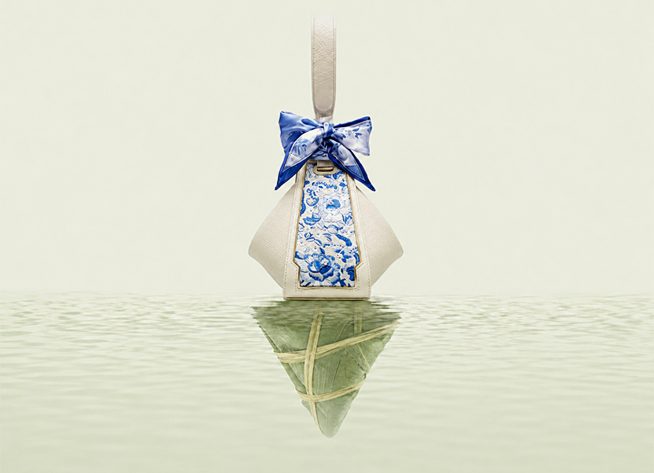 A cream SANLAN embroidered Zongzi bag with a blue silk bow reflected on calm water.