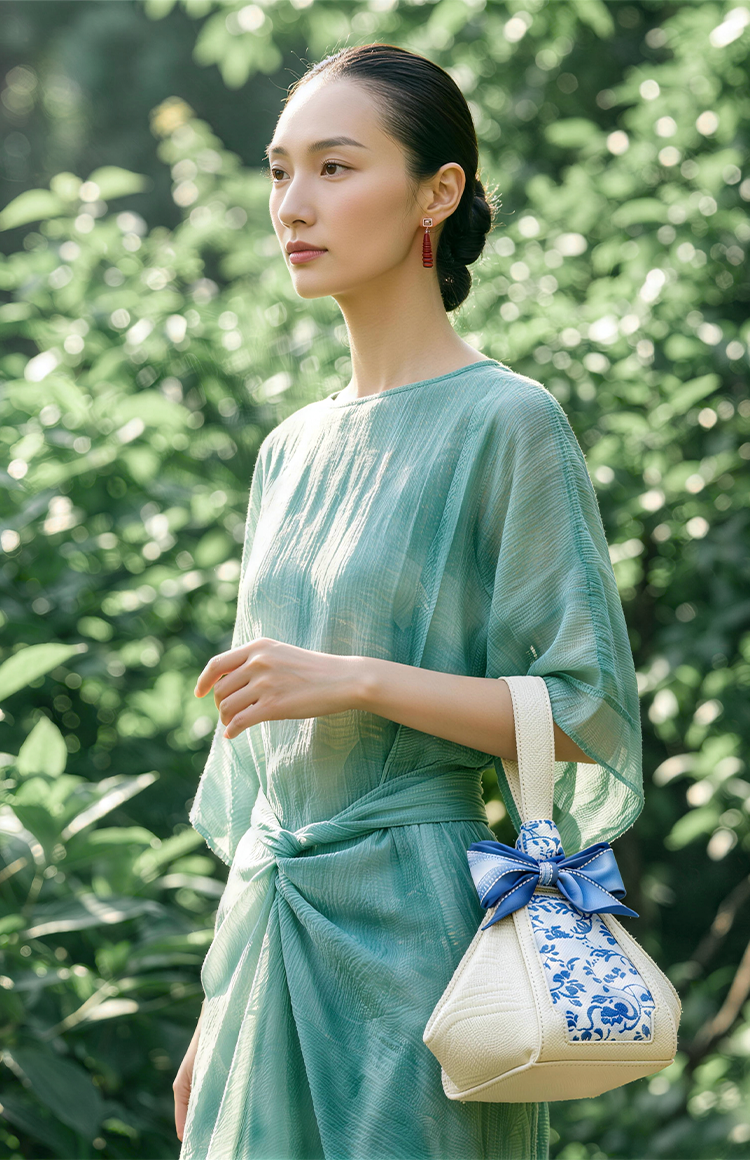 SinoCultural brand banner featuring a woman in a mint green dress carrying a cream and blue Chinese embroidered handbag in a sunlit summer garden.