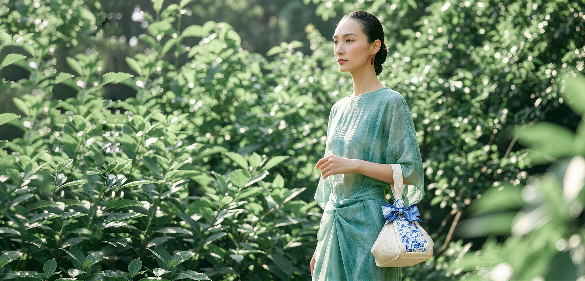 SinoCultural brand banner featuring a woman in a mint green dress carrying a cream and blue Chinese embroidered handbag in a sunlit summer garden.