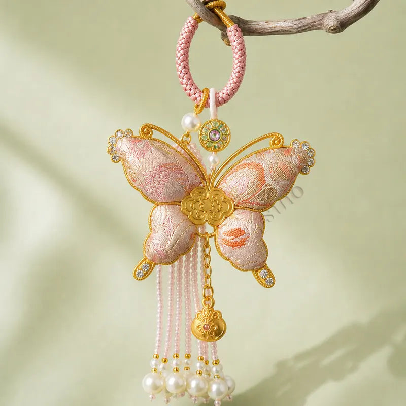 Pink Song Brocade butterfly pearl tassel bag charm hanging from a branch, featuring gold-tone trim, pearl tassels, and an auspicious butterfly motif.