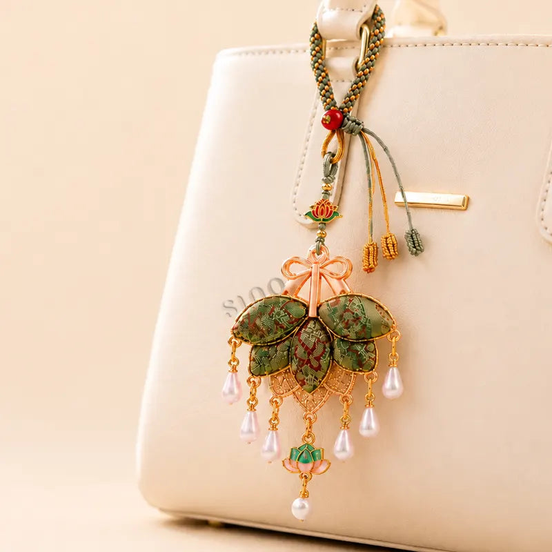 Green Song Brocade pomelo leaf tassel bag charm hanging on a light handbag with rose-gold details, lotus ornaments, and pearl-like drops.